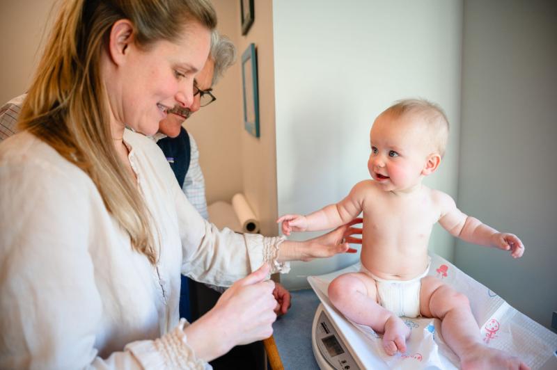 a smiling baby on an exam table with two doctors